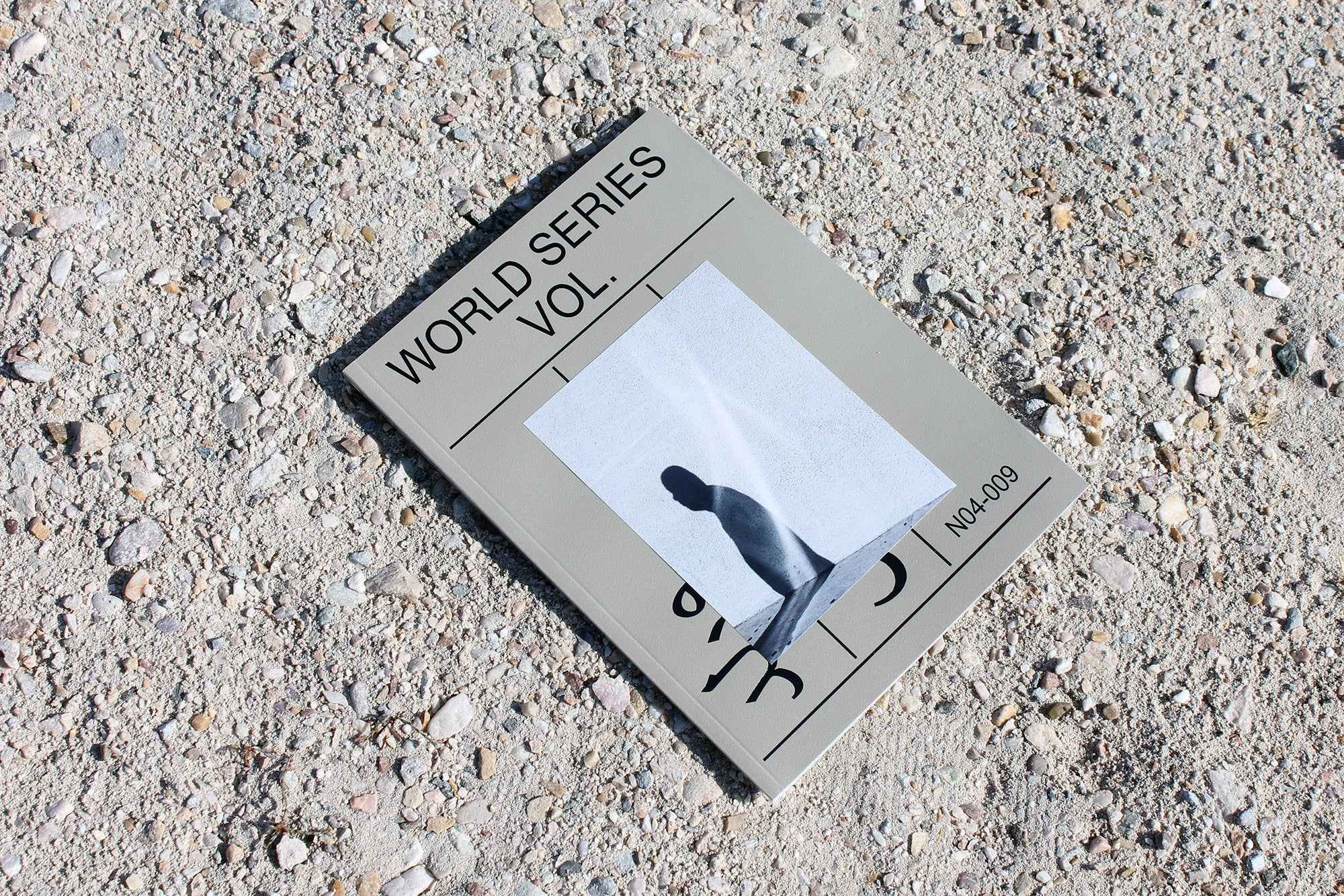 A gray World Series art and photography book on a gravel floor.