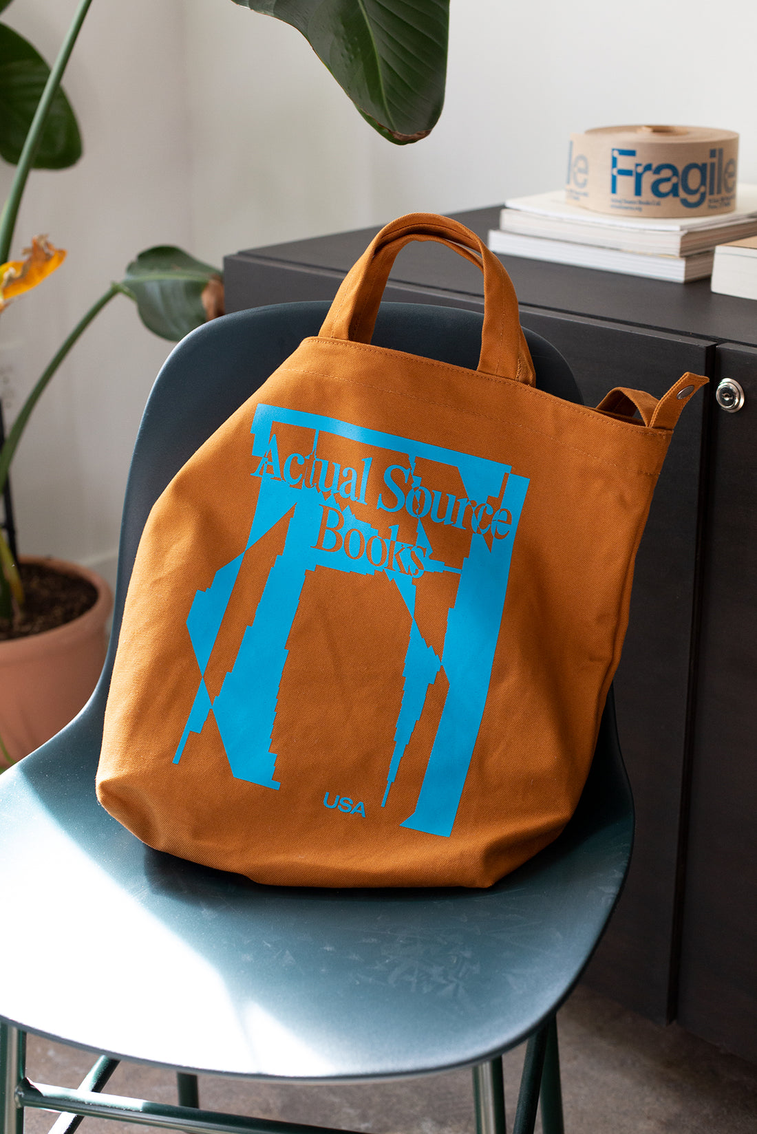 An orange and light blue tote bag sits on a modern navy chair. 