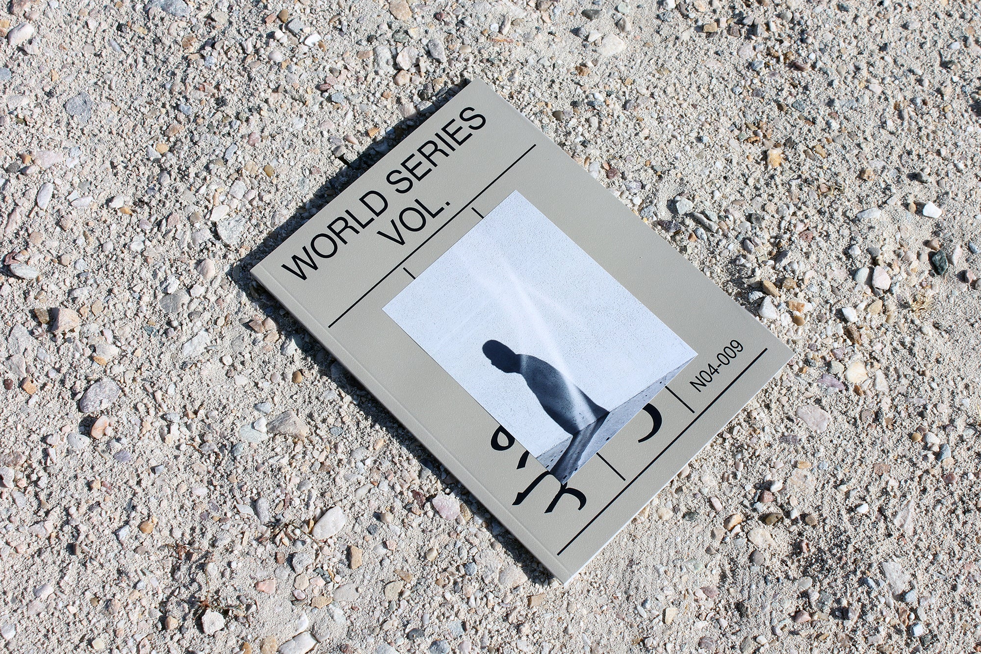 A gray World Series art and photography book on a gravel floor. 